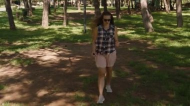 Gölgeli bir parkta yürürken kadın yukarı bakıyor güneş ışığı etrafındaki ağaçların arasından süzülüyor..