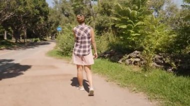 Yeşil ve Ağaçlarla çevrili Sunlit Parkı yolunda yürüyen kadın gölgeli bir bölgeye doğru ilerliyor..