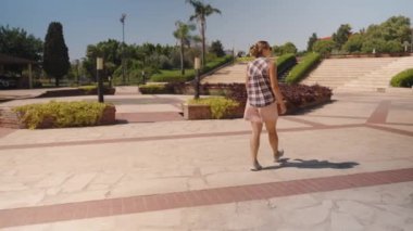 Kadın, bir şehir parkında Parlak Günışığı 'nın altında düzgünce süslenmiş çalılar ve merdivenlerle Paved Plaza' da geziniyor..