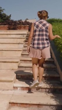 Dikey video. Kadın Stone Steps 'e doğru yürür, Green Hedge' e nazikçe dokunur, tepeye doğru tırmanırken..