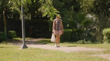 Kadın, yemyeşil ve uzun sazlıklarla çevrili bir parkta Sunlit Yolu boyunca yürüyor. Yavaş çekim.