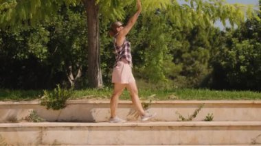 Ekose gömlekli kadın ve pembe şortlu kadın Sunlit Steps 'te dikilirken Yeşil Ağaç Dallarına doğru uzanıyor. Yavaş çekim.