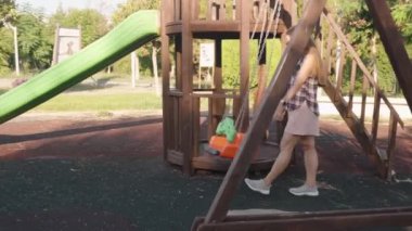 Kadın, Orange ve Green Swing 'i Tahta Oyun Yapısı ve Arkaplanda Kaydırma ile Bir Oyun Alanında Nazikçe Bastırdı.