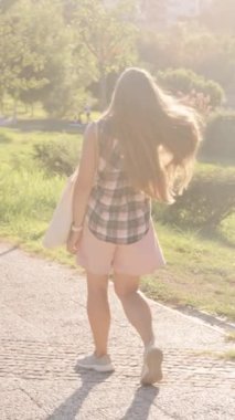 Dikey video. Güneş Işığı Gibi Yürüyen Kadın, Saçları Ayarlarken Akıyor, Yeşil ve Gölgeler Çevresini Sarmış Serene Park 'ta.