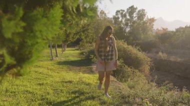 Uzaktaki Dağlar, yemyeşil ve ağaçlarla çevrili Güneş 'e batmış Çimen Bölgesi' nde Gezen Kadın.