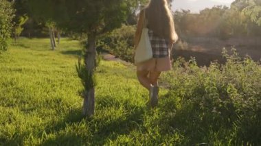 Otların üzerinde yürüyen bir kadın, ilerideki ağaçlar ve güneş ışığıyla parkın içinde huzur dolu bir gezintinin tadını çıkarıyor..