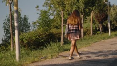 Ağaçlarla çevrili bir yol boyunca gelişigüzel bir yürüyüş. Kadının gölgesi, öğleden sonra güneşinin altında geriliyor..