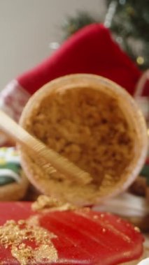 Dikey video. Boya fırçası ve parıltıyla dekore edilmiş Noel kurabiyelerinin yakın çekimi, güneşli Noel sabahı.