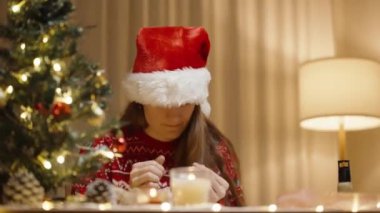 Noel Baba Şapkalı Bir Kadın ve Kırmızı Şenlikli Süveter Ustalıktan, Saçlarını Sıcak Bir Ev Ortamına Atmaktan Hoşlanıyor.