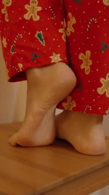 Dikey video. Kırmızı Şenlikli Süveter Giyen Bir Kadın Perdeye İp Işıklarını Asıyor, Sıcacık Evine Bir Işıltı Ekliyor.
