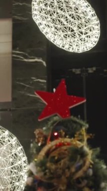 Dikey video. Noel ağacının tepesini çevreleyen parlak ışık küreleri çarpıcı bir görüntü oluşturuyor..