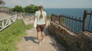 Taş Yolda Yürüyen Kadın, Okyanusa Bakan, Güneşli bir günde Rocky Duvarları ve Demir Çit ile çevrili.