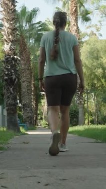 Dikey video. Geriye Bakış, Avuç İçi Çizgisi Üzerinde Yürüyen Kadın, Mavi Benç Geçişi, Yeşillik Çevreleme, Açık Gökyüzü ile Parlak Gün.