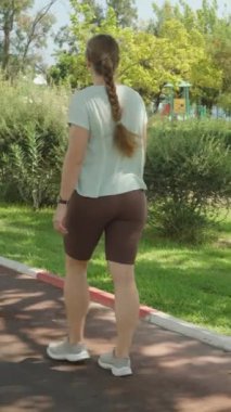 Dikey video. Çevresi Yeşil Çimler ve çalılarla çevrili, Solunda Mavi Bisiklet Yolu, Parlak ve Güneşli Gün.