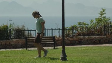 Oceanfront Park 'a Yakın Yürüyen Kadın, Yeşil Çim Ayak Altında, Demir Çit, Lamba Post ve Huzurlu Bir Sahne Oluşturan Uzak Dağlar.