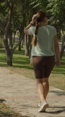 Dikey video. Yakınlaştır, Park 'ta Kadın Yürüyor, Ağaçlar ve Kayalarla çevrili, Piknik Alanı Görünür, Sakin ve Güneşli Gün.