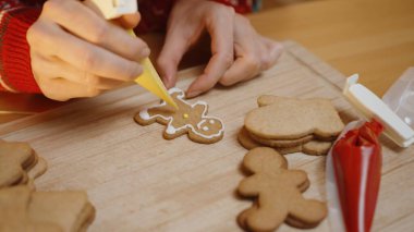 Elleri, diğer sade kurabiyeler ve buzlu poşetlerle çevrili Tahta Tahtadaki Sarı Buzlu Zencefilli Kurabiye Adam Kurabiyesine Devam Ediyor.