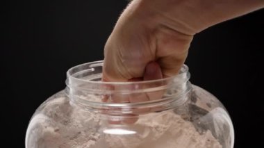 Sporcu, konteynırın üzerinde bir kepçe dolusu Protein tozu tutuyor ve egzersiz sallaması için gereken miktarı ölçmeye hazırlanıyor. Yavaş çekim.