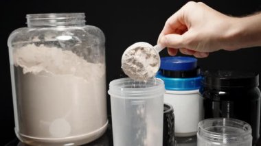 Sporcu, protein tozunu şişeye boşaltıyor, egzersiz sonrası beslenme artışı için karıştırmaya hazır. Yavaş çekim.