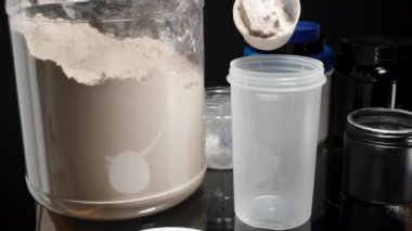 Sporcu bir kepçe Protein tozunu karıştırıcı şişeye boşaltıp besin açısından zengin bir egzersiz sonrası içeceği hazırlıyor. Yavaş çekim.