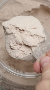 Dikey video. Protein tozunu büyük bir konteynırdan kepçeleyen bir sporcunun üst görüntüsü karışıma katkı maddesini hazırlıyor. Yavaş çekim.