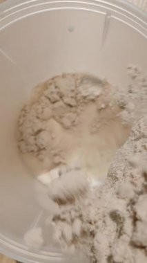 Dikey video. Çalkalayıcıdaki süte bir kepçe çikolatalı protein tozu ekliyoruz. Kamera karışımı yakalamak için içeri iniyor. Dolly Slider, kapat. Yavaş çekim.