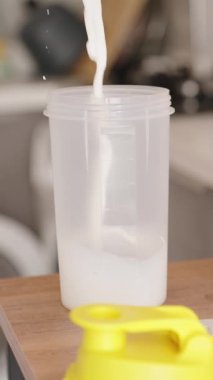 Dikey video. Büyük bir kutu Protein tozunun yanına süt dökerek, bir milkshake hazırlıyorum..