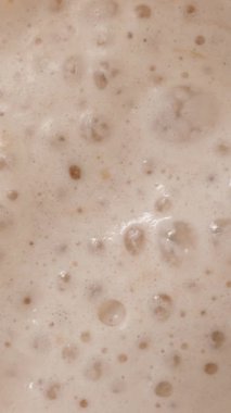 Dikey video. Protein Shake köpüğünde kabarcıkların kabarcıklarının patlaması içkinin zenginliğini ve tutarlılığını vurguluyor..
