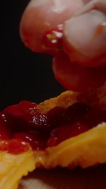 Dikey video. Acı Kavun 'dan Parlak Kırmızı Tohum Tutan Parmaklar, Sulu Dokuları Gösteriyor ve Karanlık Arkaplan Karşısında Canlı Renkler.