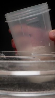Dikey video. Bir el, Protein tozuyla dolu bir Shaker bardağına bir ağ süzgeci yerleştirir ve karıştırmaya hazırlanır..