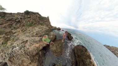 Bir adam ve bir kadın etraflarındaki dalgalar çarptığında kaygan kayalıklarda dururlar. Sahne, engin denizi ve kayalıkları gösteren 360 'lık bir manzarayla çekilir..