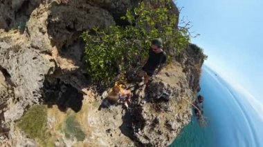 Bir adam ve bir kadın okyanusa bakan bir uçurum kenarında yürüyorlar. Video yukarıdan çekiliyor, dar yol boyunca hareketlerini ve aşağıdaki geniş deniz manzarasını yakalıyor..