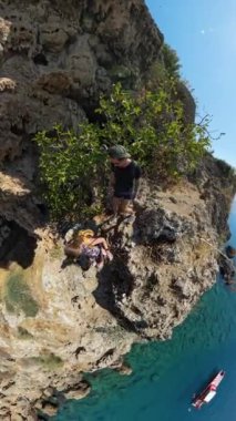 Dikey video. Bir adam ve bir kadın okyanusa bakan bir uçurum kenarında yürüyorlar. Video yukarıdan çekiliyor, dar yol boyunca hareketlerini ve aşağıdaki geniş deniz manzarasını yakalıyor..