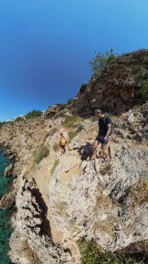 Dikey video. 360 derecelik kamera ile bir adam ve bir kadın denizin üzerinde dar bir uçurum kenarında yürüyorlar. Video geniş açıyla çekiliyor. Dik düşüş ve aşağıdaki sudaki tekneyi gösteriyor..