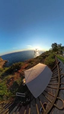 Dikey video. Küçük Tahta Ev 'e yaklaşan Bir Kedinin Yakın Çekimi, Küçük Gezegen Manzaralı Okyanusa Bakan Bir Kadın Gözlemliyor,.