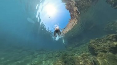 Rocky Deniz yatağı boyunca yüzen bir adam, yüzeye doğru gidiyor. Sahne aşağıdan yukarıya doğru çekiliyor, derinliği ve suyun içindeki güneş ışığını vurguluyor..