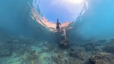 Bir adam sualtı mağarasında ışığa doğru hızla yüzer, Geniş ve geniş bir açıyla yakalanır..