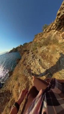 Dikey video. Rocky Cliffside Yolu 'na Tırmanan Bir Kadın İlk Kişi Görünümü, Aşağıdaki Güneş Işığı Okyanusu ve Kıyı Manzarası' na Bakış.