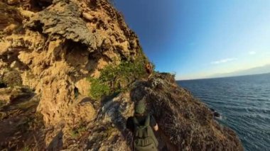 Dar Kıyı Yolunda Yürüyen Bir Adam, Bir tarafında uçurumlar ve diğer tarafında okyanustan yansıyan altın gün batımı.