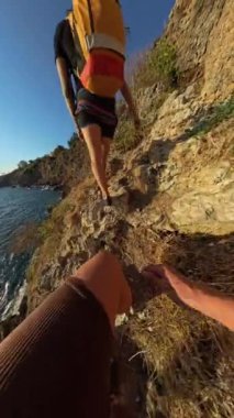 Dikey video. Dar Kayalıklar 'a tırmanan Önde Önde Bir Erkek, Uçurumda Yalınayak Yürüyüşü, Altında Parıldayan Okyanus.