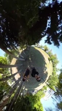 Dikey video. Küçük Gezegen 'de ağaçlarla çevrili genç bir adam ve kadını ağaçların tepesindeki gölgeler ve ışığın karışımı ile dairesel bir dünya benzeri bir etki yaratıyor..