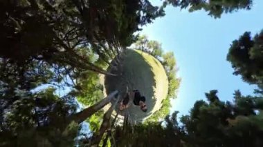 Küçük Gezegen etkisi, ağaçların içe doğru eğildiği, küresel bir illüzyon yaratan, çifti ve çevresini çevreleyen yeşilliği vurgulayan ormanlık bir alanda genç bir adam ve bir kadın üzerinde..