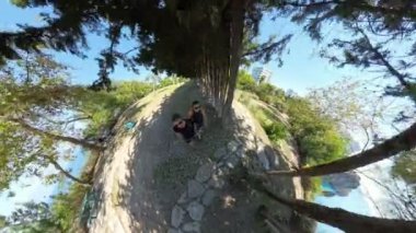 Deniz kenarında yaşayan genç bir çiftin küçük gezegen etkisi. Ağaçların altında duruyorlar. Arka planda çarpıcı bir okyanus manzarası var..