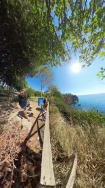 Dikey video. Deniz kenarında genç bir çiftin 360 panorama etkisi. Ağaçların altında duruyorlar. Arka planda çarpıcı bir okyanus manzarası var..