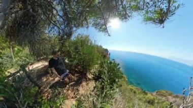 Kaktüs yakınlarında dinlenen bir adamın geniş açılı manzarası, arka planda parlak güneş ve okyanus, kıyı manzarasının doğal güzelliğini gösteriyor..