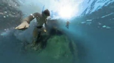 Küçük gezegen. Bir adamın su altında kayalıklardan derinlere dalışının görüntüsü, suyun derinliklerine dalarken, güneş ışığı yüzeyden süzülüyor, alçalmayı ve etrafındaki kayaları aydınlatıyor..