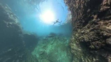 360 derecelik Panorama Snorkeler, kayalık oluşumların yakınında süzülen dalgıç, berrak suda parlayan güneş ışığıyla büyük bir su altı kayasının çevresini keşfediyor..