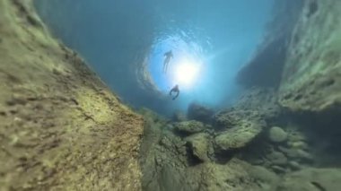 Snorkeller, su yüzeyinde parlayan parlak bir güneşle kayalık deniz tabanını keşfediyor. Çevredeki kayaları aydınlatıyor ve derinlik hissi yaratıyorlar..