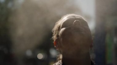 Yüzü yukarıya doğru eğilmiş, etrafı sis ve güneş ışığıyla çevrili, dingin ve manevi bir etki yaratan bir kadın. Düşük açı ve hafif ışıklandırma bir huzur ve rahatlama anını vurguluyor..