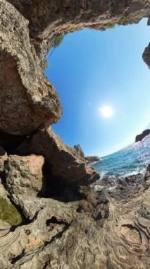 Dikey video. 360 derece kamera. Güneşe doğru bakan iki kayalık uçurum arasından bir manzara. Güneş ışığı engebeli araziden yansıyarak doğal manzarayı aydınlatıyor. Sahnenin geniş açılı görüntüsü..